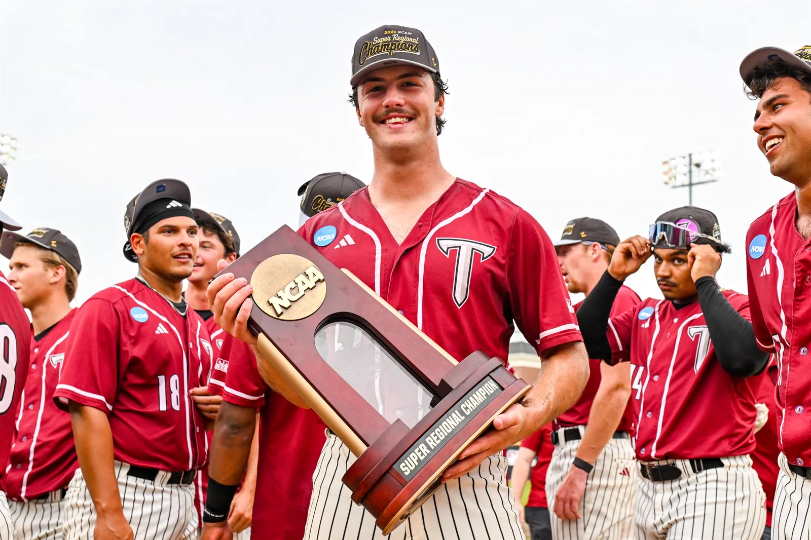 Dylan Alonso holding the NCAA Super Regional Champion trophy with teammates